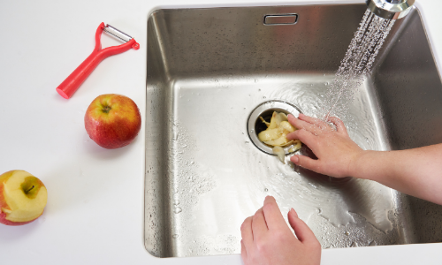 Hands pushing food scraps into kitchen sink drain